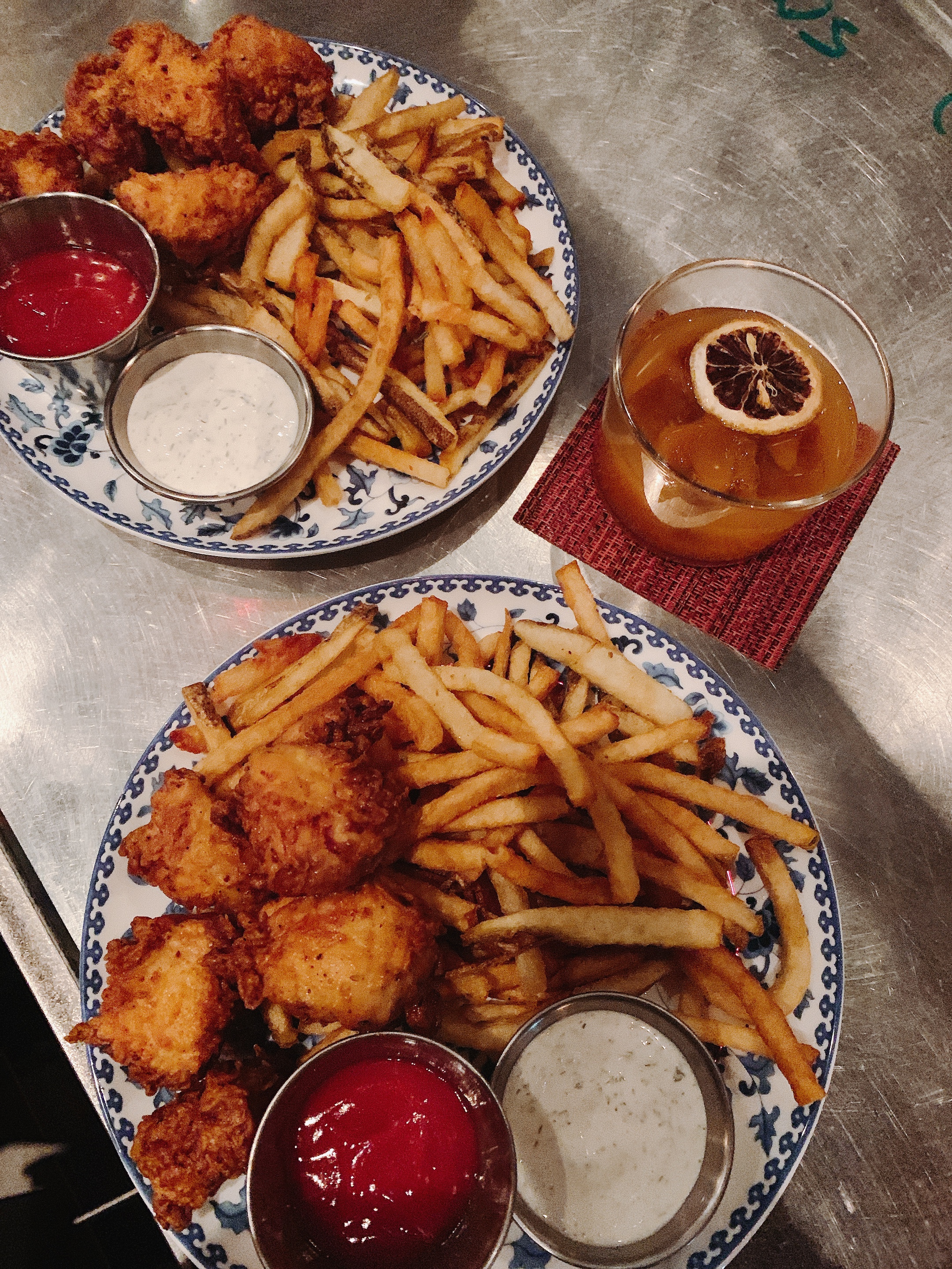 two plates of chicken, fries, and drinks